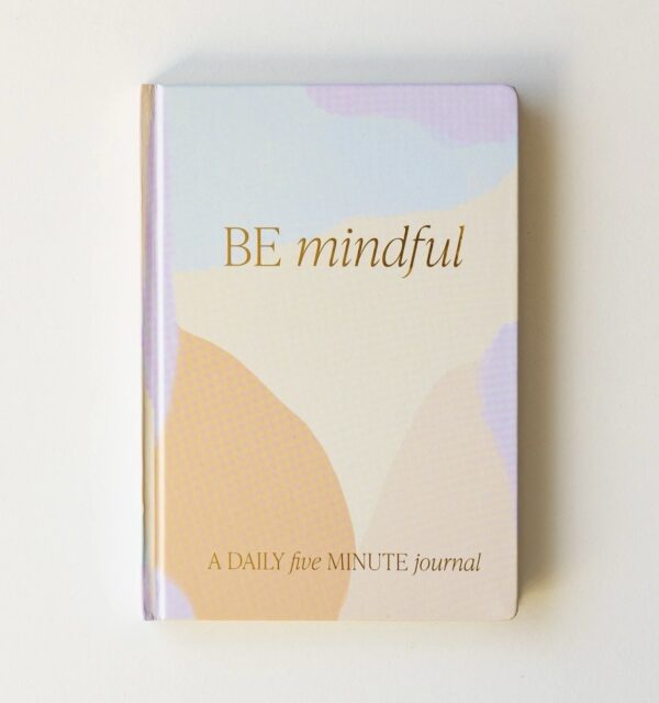 A journal with a pastel abstract cover features the text "BE mindful" and "A DAILY five MINUTE journal.
