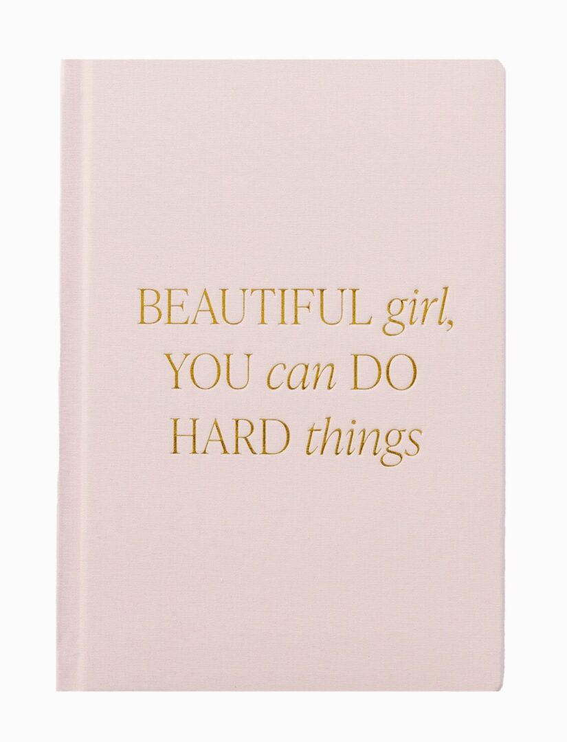 A beige notebook with gold text saying, "Beautiful girl, you can do hard things.