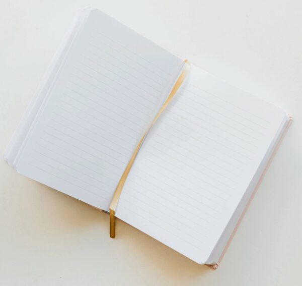 The Beautiful Girl Fabric Journal lies open, revealing its lined pages with a golden ribbon bookmark elegantly draped diagonally across them, all set against a light backdrop.
