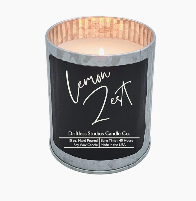 A lit candle labeled "Lemon Zest" from Driftless Studios Candle Co., in a silver metal container. Burn time is 40 hours, 10 oz, hand-poured soy wax, made in the USA.