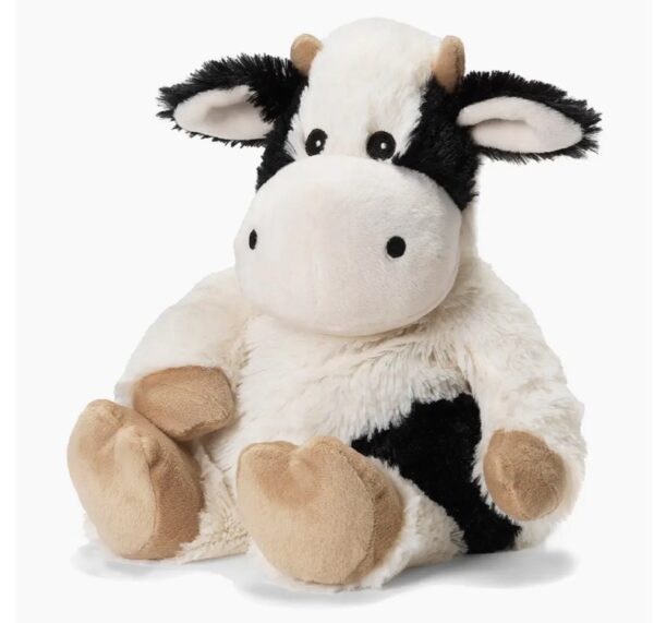 The Black And White Cow Warmie is a plush toy with black and white fur, tan hooves, and large round eyes, sitting upright against a white background.