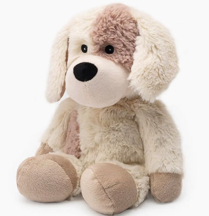 A plush toy dog with beige and white fur, brown spots, large floppy ears, and a black nose sits upright.