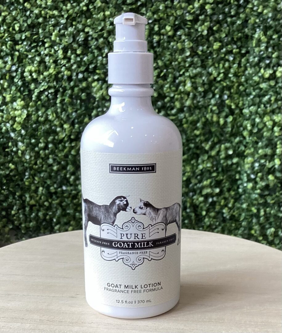 Bottle of Beekman 1802 Pure Goat Milk Lotion, fragrance-free formula, placed on a wooden surface with a leafy green background.
