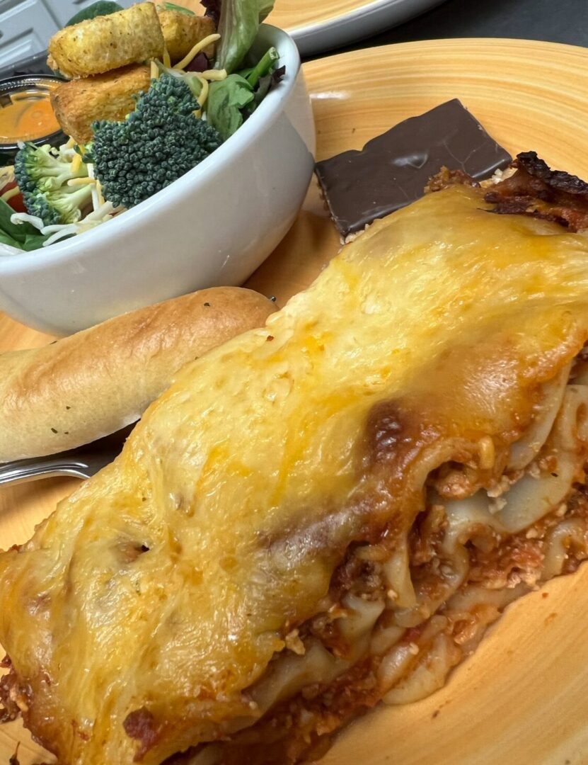 A serving of the Lasagna Dinner on a wooden plate, complete with a side salad, breadstick, and a piece of chocolate.