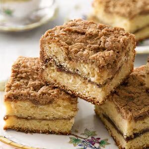 Three square slices of Granny's Coffee Cake stacked on a decorative plate, featuring layers of cinnamon and a crumb topping.